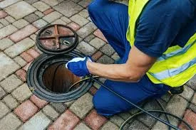 Technician inspecting open storm drain in asphalt surface with cleaning equipment