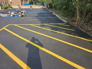 Freshly sealed asphalt parking lot with bright yellow parking space lines and directional markings