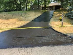 Newly sealcoated asphalt driveway with dark finish, residential property with landscaping
