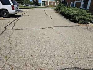 Asphalt driveway with visible cracks and surface damage before repair