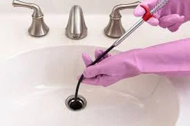 Technician cleaning sink drain with specialized tool and pink cleaning solution