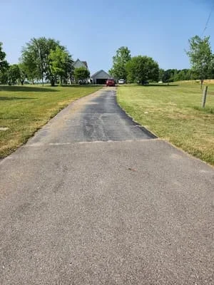 Newly paved asphalt driveway with dark aggregate surface and grass borders