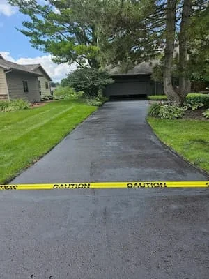 Freshly sealed asphalt driveway with dark black finish, mature trees and lawn visible