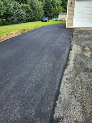 Newly paved black asphalt driveway next to garage with white door
