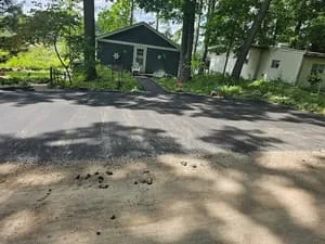 Cracked and worn asphalt driveway with patching needs visible near residential home