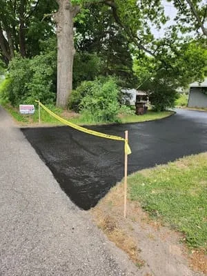 Freshly sealcoated driveway with yellow caution tape marking wet asphalt