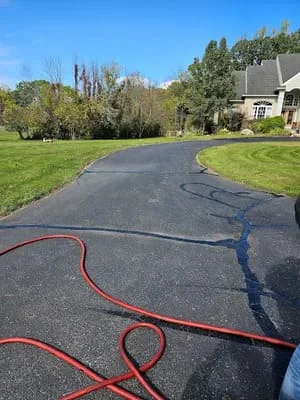 Sealed asphalt driveway with red hose and equipment, curved residential drive